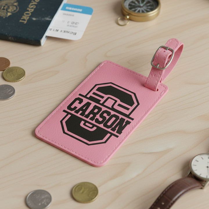 Pink luggage tag with 'CARSON' name engraved sitting on a wooden surface with coins, watch, and passport.