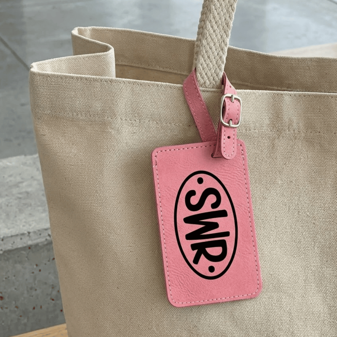 Beige tote bag with a pink luggage tag featuring 'SWR'  monogram engraved in black on a concrete floor background