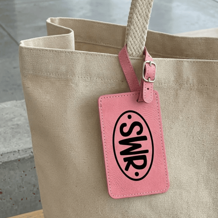 Beige tote bag with a pink luggage tag featuring 'SWR'  monogram engraved in black on a concrete floor background