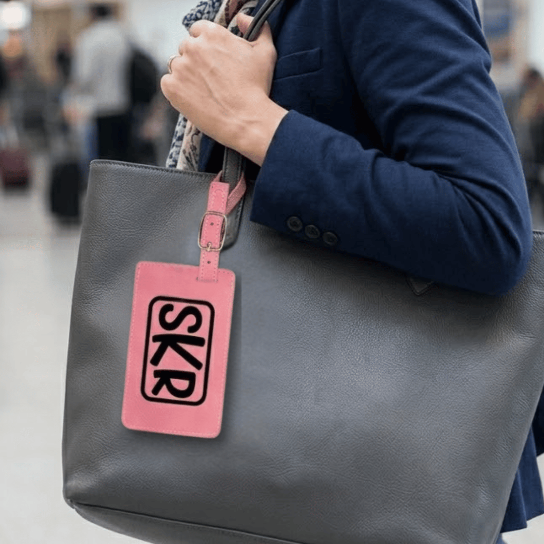 Person holding a gray bag with a pink tag featuring 'SKR' engraved monogram on a blurred background