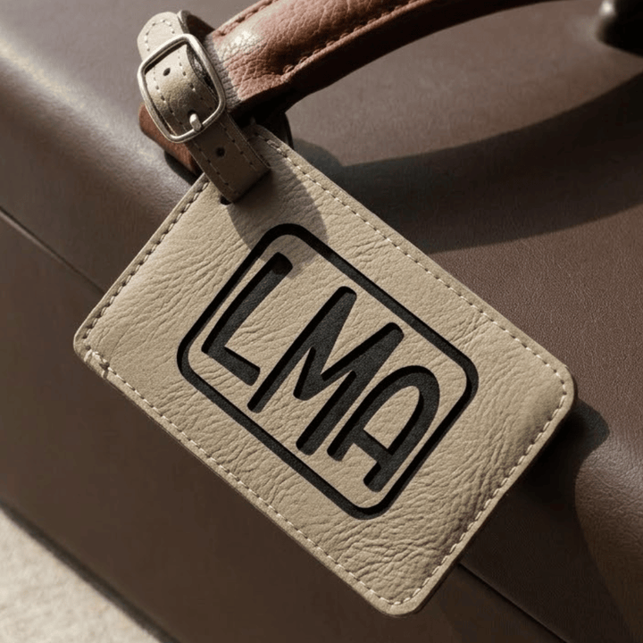 Leather luggage tag with 'LMA' engraved in black on a brown suitcase