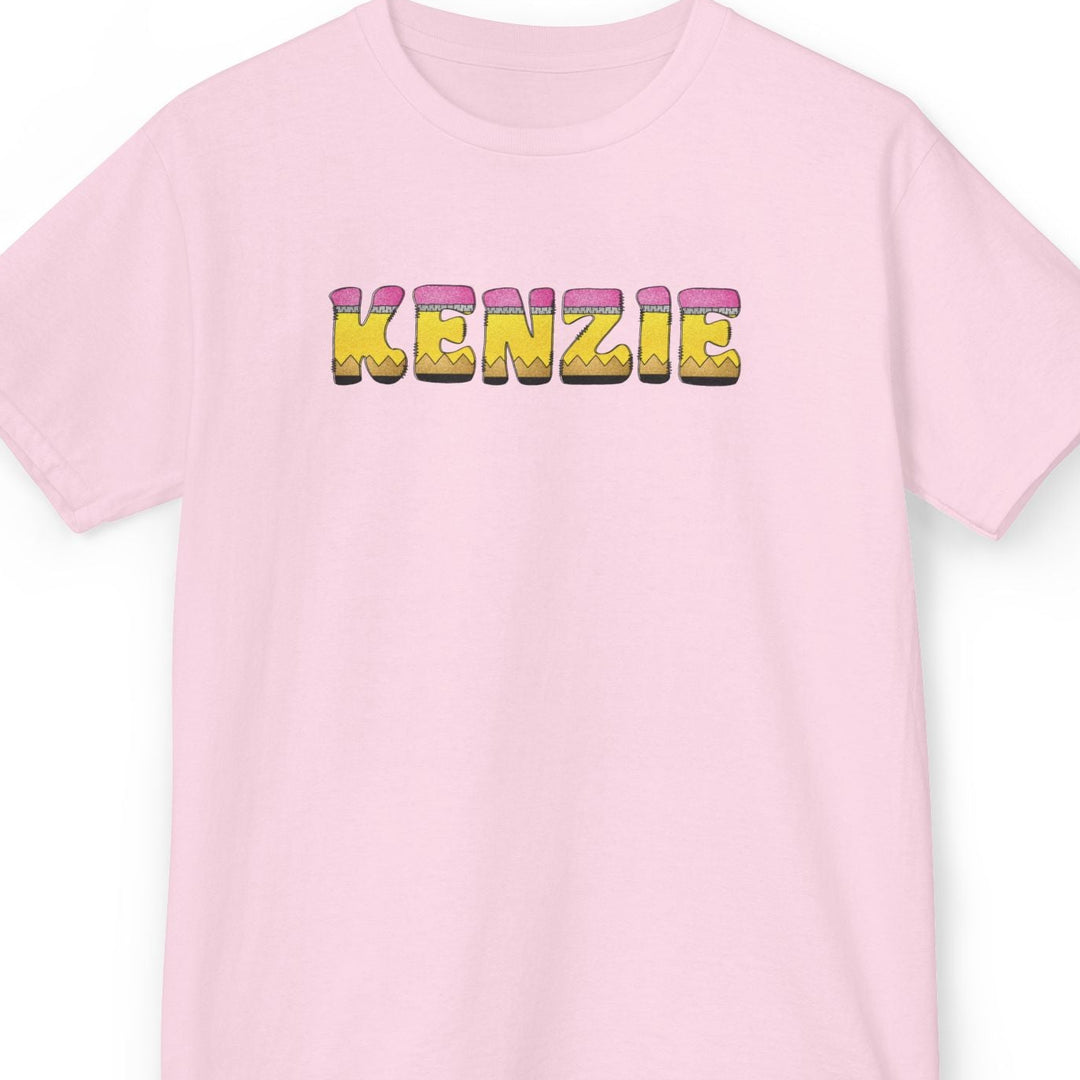 A light pink short-sleeve crewneck t-shirt featuring the name 'KENZIE' printed across the chest in 3D pencil letters font.