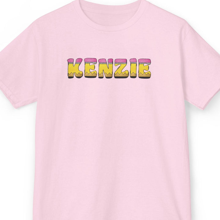 A light pink short-sleeve crewneck t-shirt featuring the name 'KENZIE' printed across the chest in 3D pencil letters font.