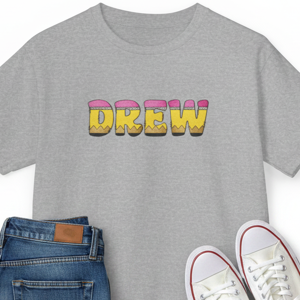 A heather gray short-sleeve t-shirt with pencil letters graphic spelling 'DREW', styled in a flat lay on a white background next to white sneakers and jeans.