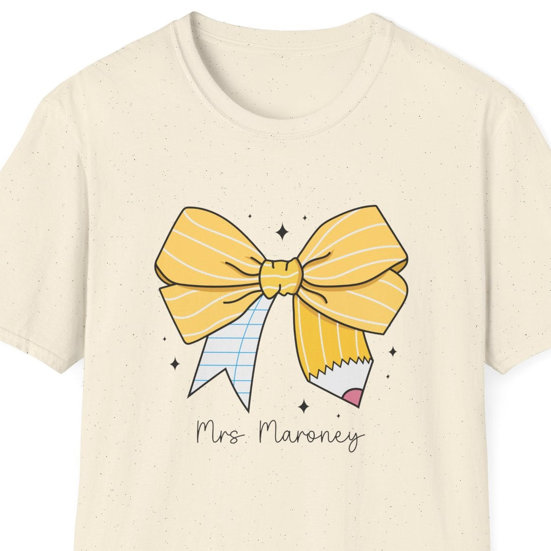 An off-white short-sleeve crewneck t-shirt featuring a cartoon graphic of a yellow striped bow, a pencil, and the text 'Mrs. Maroney' printed on the front.