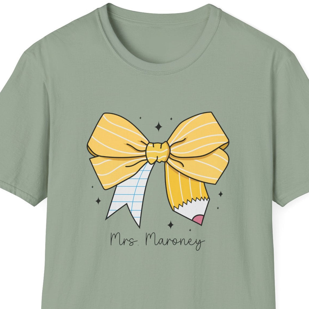 A sage green short-sleeve t-shirt with a graphic of a yellow striped bow, a pencil, and the text 'Mrs. Maroney' printed on the front, shown against a plain white background.
