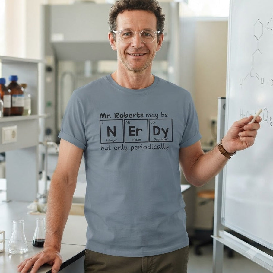 A man in a chemistry lab wearing a light blue t-shirt with a periodic table graphic that reads 'Mr. Roberts may be N Er Dy but only periodically'.