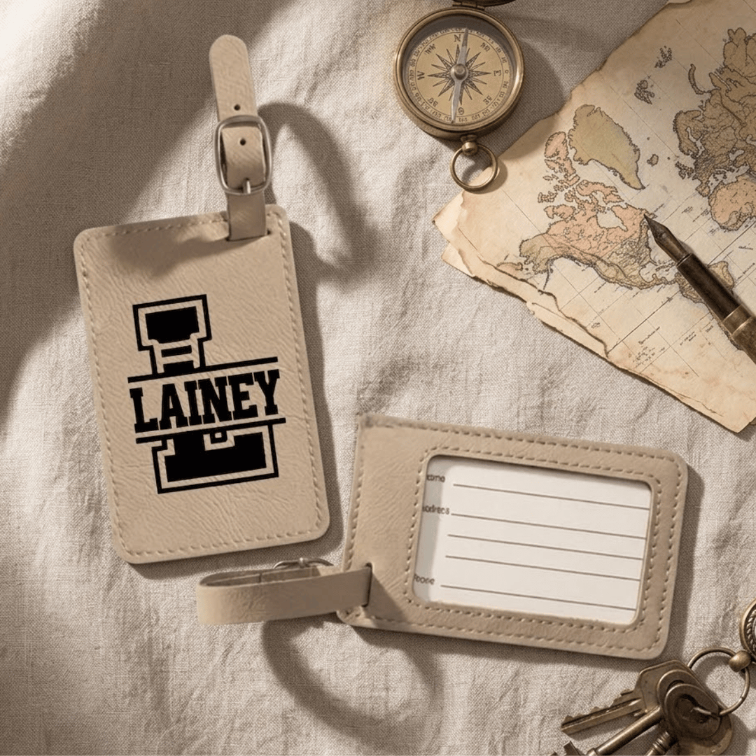 Two beige luggage tags on a textured surface with a world map and compass in the background. Front has a varsity style split monogram engraved in black. The back shows a clear plastic opening with a removable card for personal information.