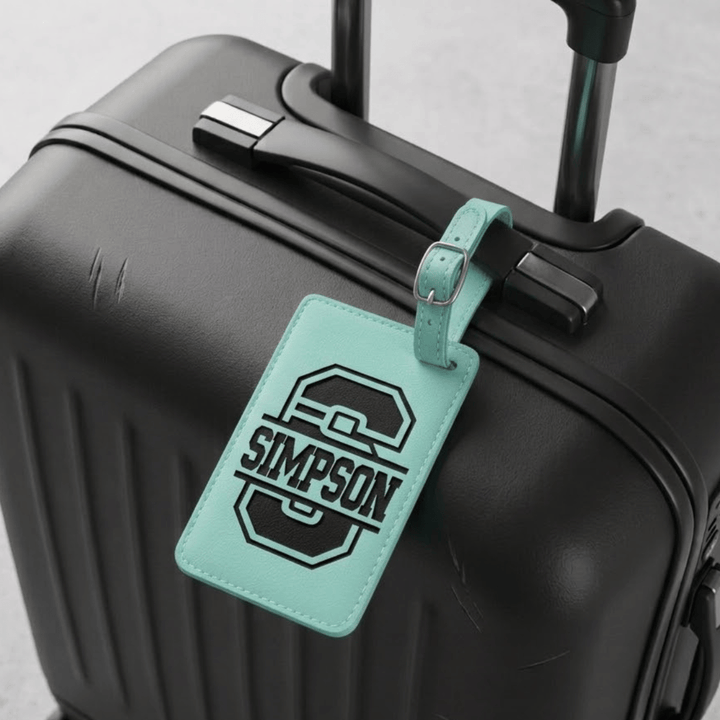 Black suitcase with a teal luggage tag featuring the engraved monogram 'Simpson'.