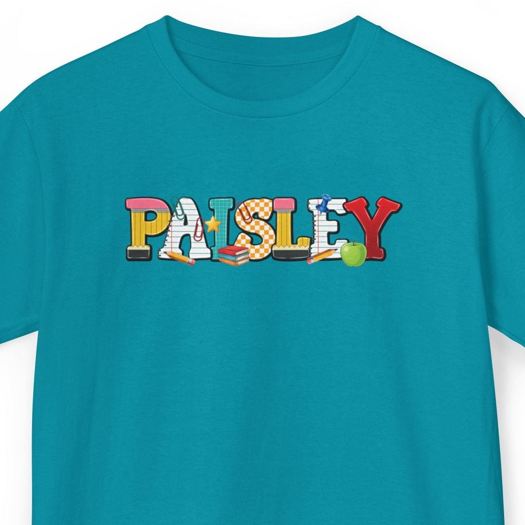 A teal short-sleeve t-shirt with the word 'PAISLEY' printed across the chest in a colorful, playful font featuring school supplies, shown on a plain white background.