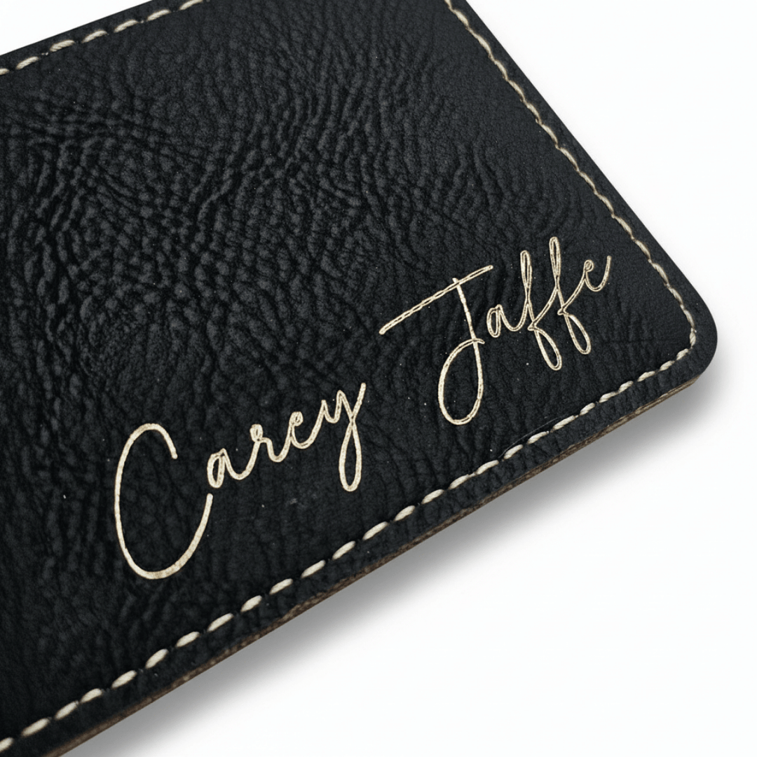 Black textured leather luggage tag with 'Carey Jaffe' engraved in metallic gold, laying on a white background