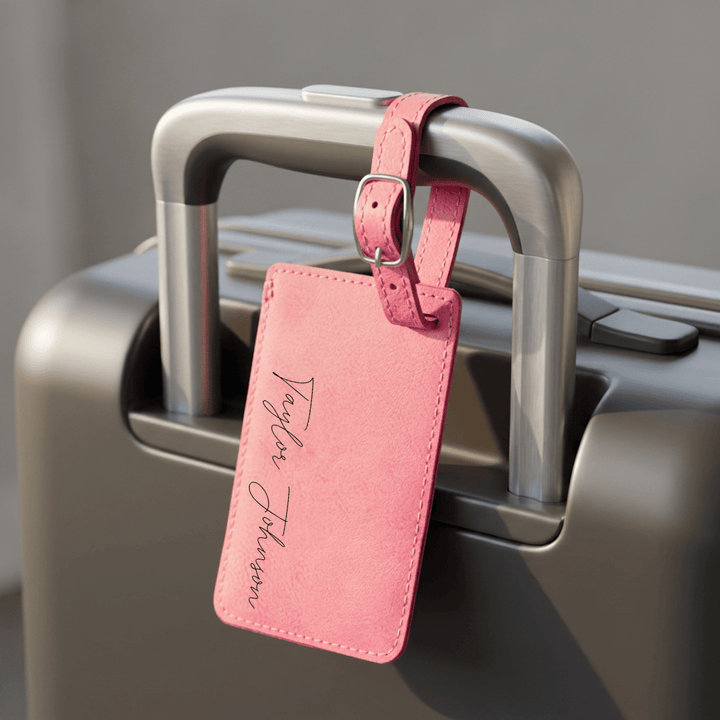 Pink luggage tag attached to a suitcase handle with a blurred background