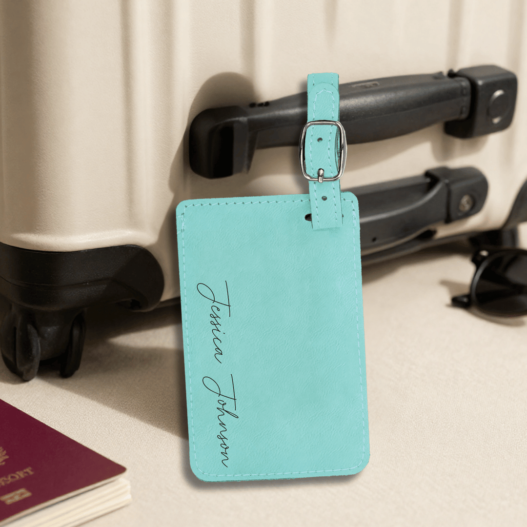 Teal luggage tag with name engraved in black modern script hanging on a suitcase