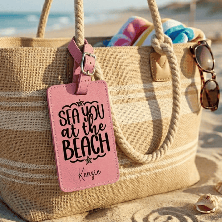 Beach bag with pink 'Sea you at the Beach' tag on a sandy background