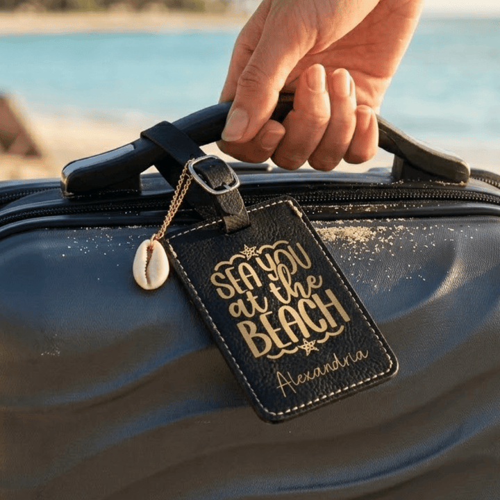 Hand holding a suitcase with a 'Sea you at the Beach' luggage tag against a beach background.