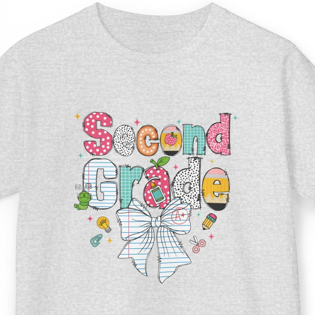 A light ash gray short-sleeve t-shirt with a colorful 'Second Grade' school graphic on the chest, featuring a striped bow, polka dots, and school-themed doodles, shown against a plain white background.