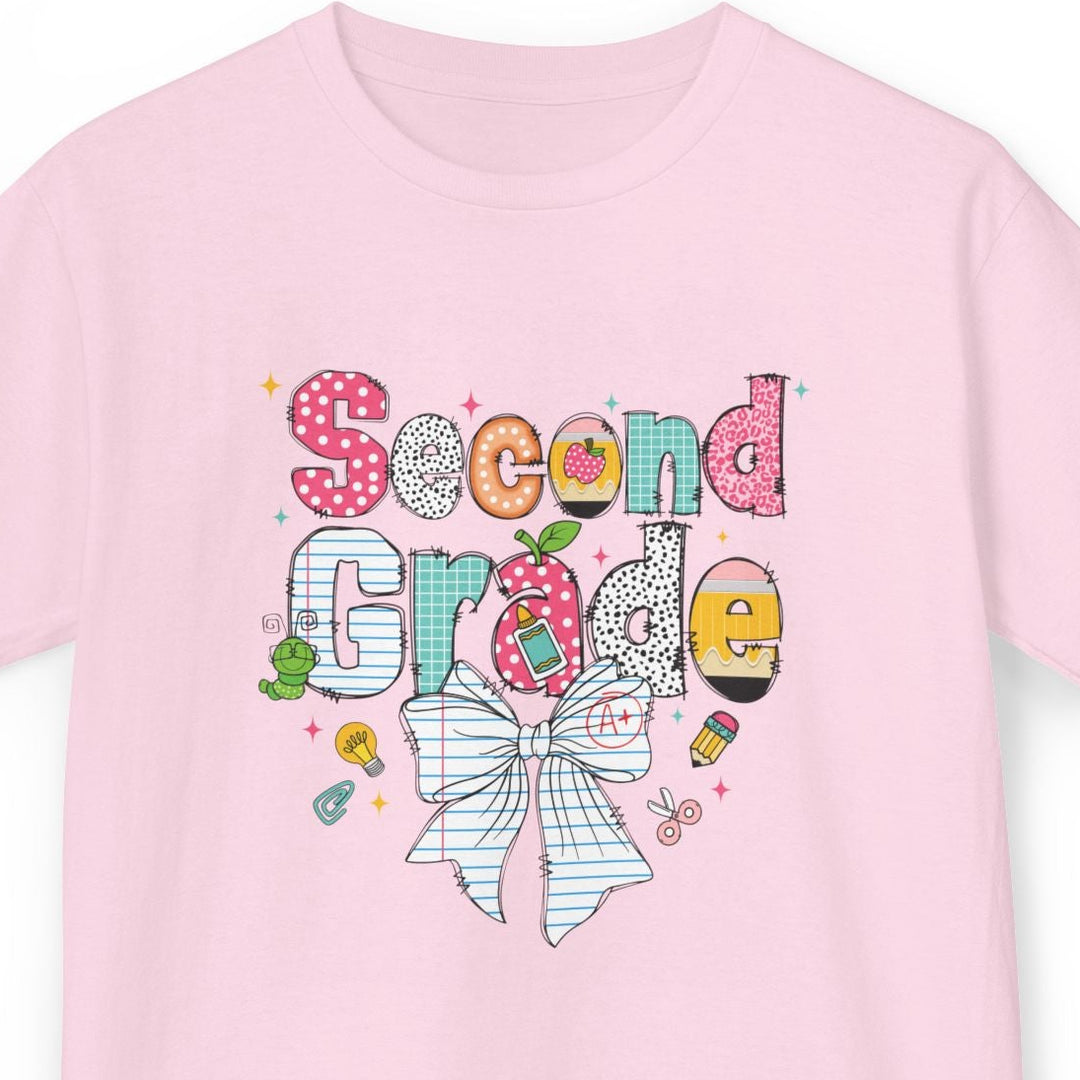 A light pink short-sleeve t-shirt with a colorful 'Second Grade' birthday graphic on the front, featuring a striped bow, polka dots, and school-themed doodles, shown against a plain white background.