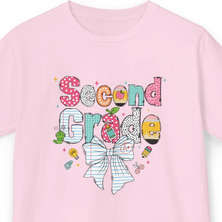 A light pink short-sleeve t-shirt with a colorful 'Second Grade' birthday graphic on the front, featuring a striped bow, polka dots, and school-themed doodles, shown against a plain white background.