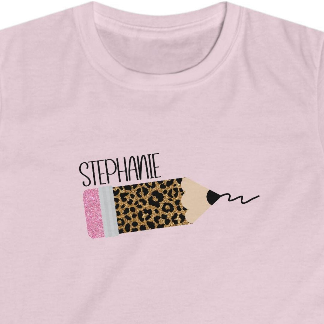 A light pink short-sleeve t-shirt with a custom leopard print pencil graphic on the chest. The graphic features the name 'STEPHANIE' in black script above a pencil illustration with a leopard print body, a pink eraser, and a black scribble.