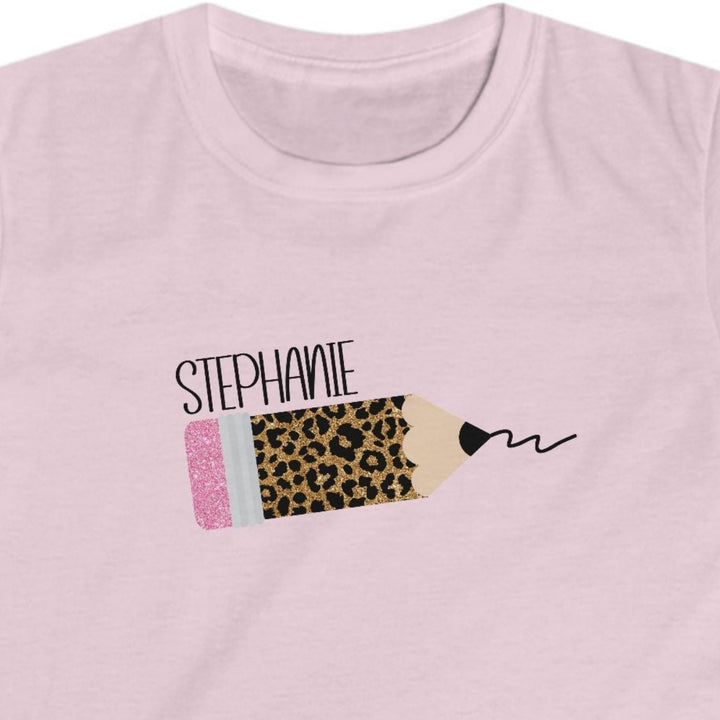 A light pink short-sleeve t-shirt with a custom leopard print pencil graphic on the chest. The graphic features the name 'STEPHANIE' in black script above a pencil illustration with a leopard print body, a pink eraser, and a black scribble.