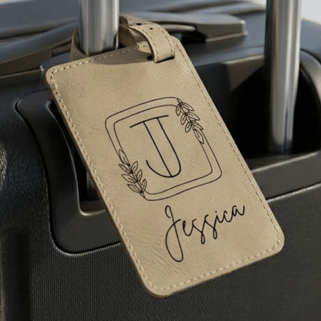 Beige luggage tag with floral monogram and name engraved in black attached on a suitcase