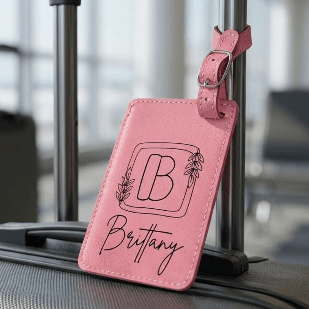 Pink luggage tag with 'B' and 'Brittany' engraved text on a suitcase.