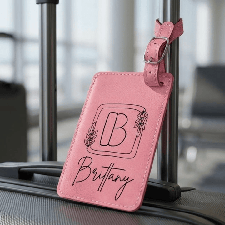 Pink luggage tag with 'B' and 'Brittany' engraved text on a suitcase.