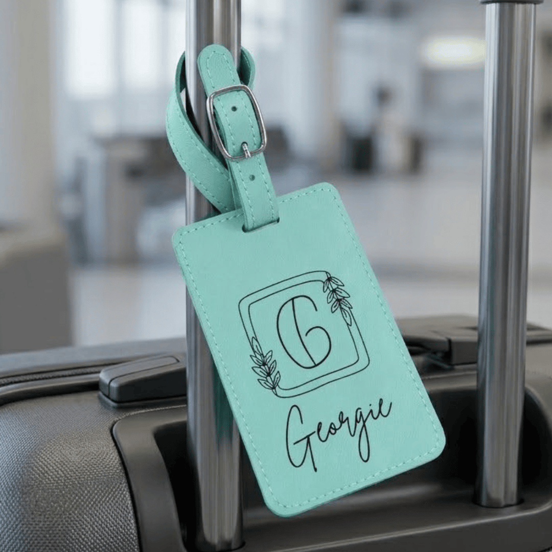 Mint green luggage tag with 'Georgie' engraved laying on a suitcase handle.