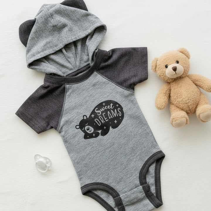 A baby short-sleeve bodysuit with an attached hood. The bodysuit has heather gray and dark gray raglan sleeves and trim, with a black graphic on the chest reading &