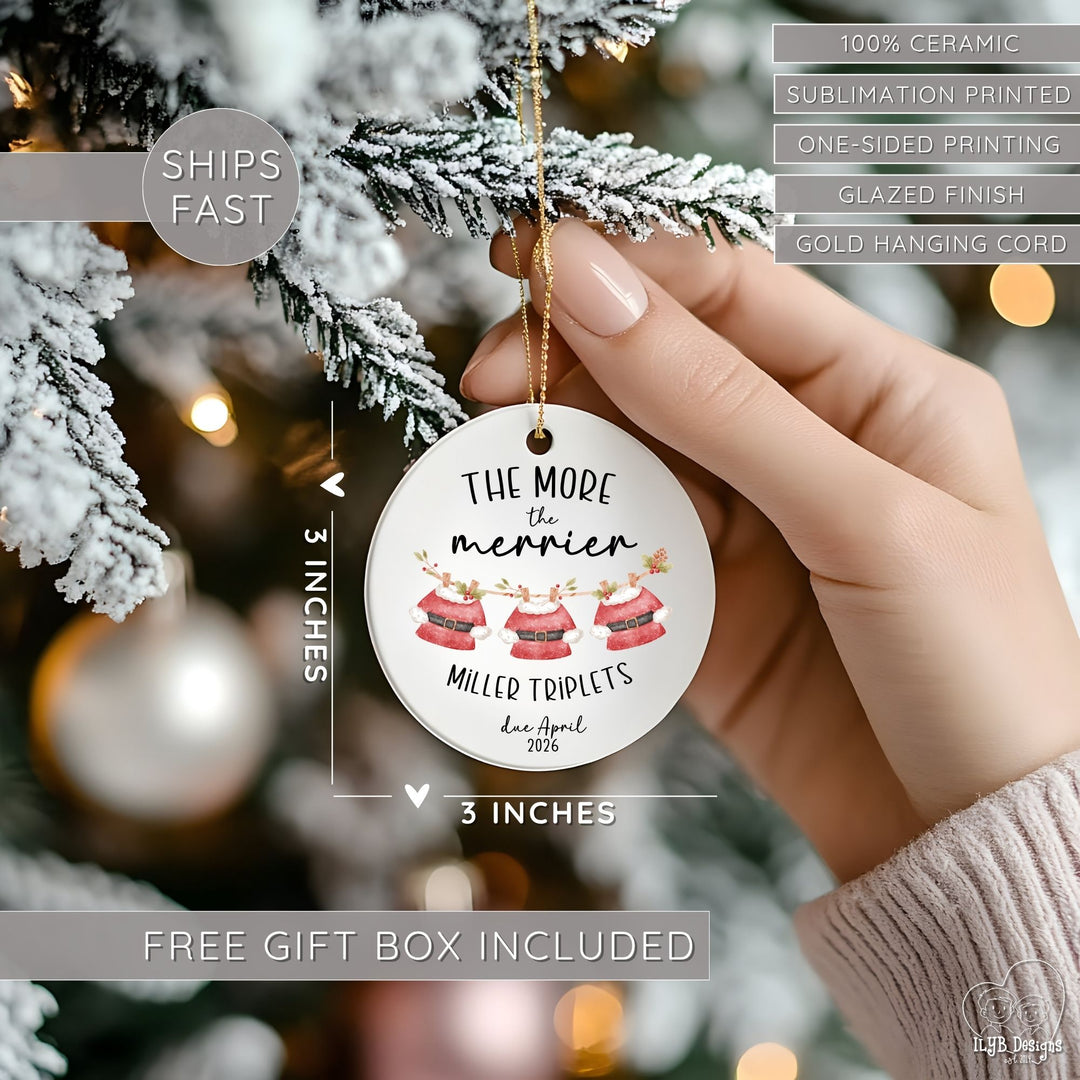 Hand hanging "The more the merrier" ornament on a Christmas tree and showing dimensions of the ornament in perspective next to the hand. Ornament dimensions are 3 inches x 3 inches. Other features are highlighted: 100% ceramic, sublimation printing, one-sided print, glazed finish, gold hanging cord, free gift box included, ships fast.