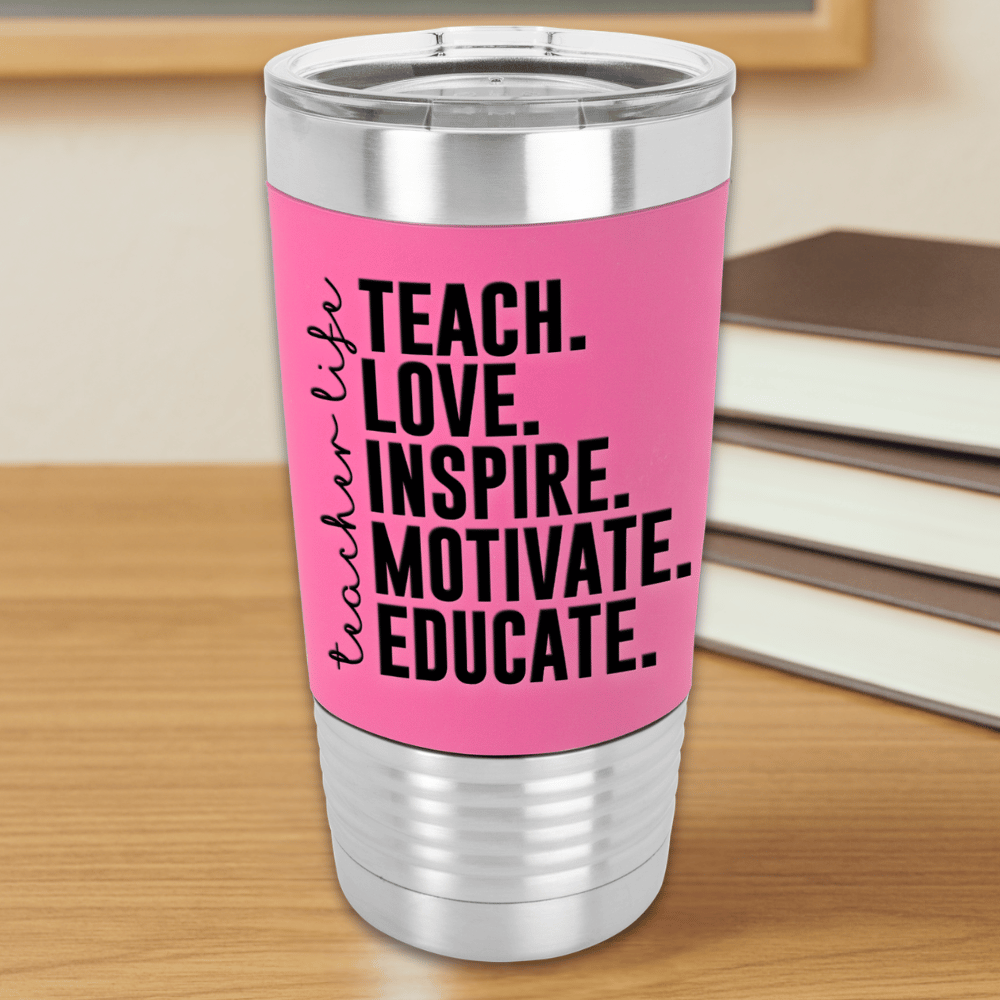 Pink tumbler with motivational teacher quote, 'teach, love, inspire, motivate, educate, teacher life' sitting on a wooden surface