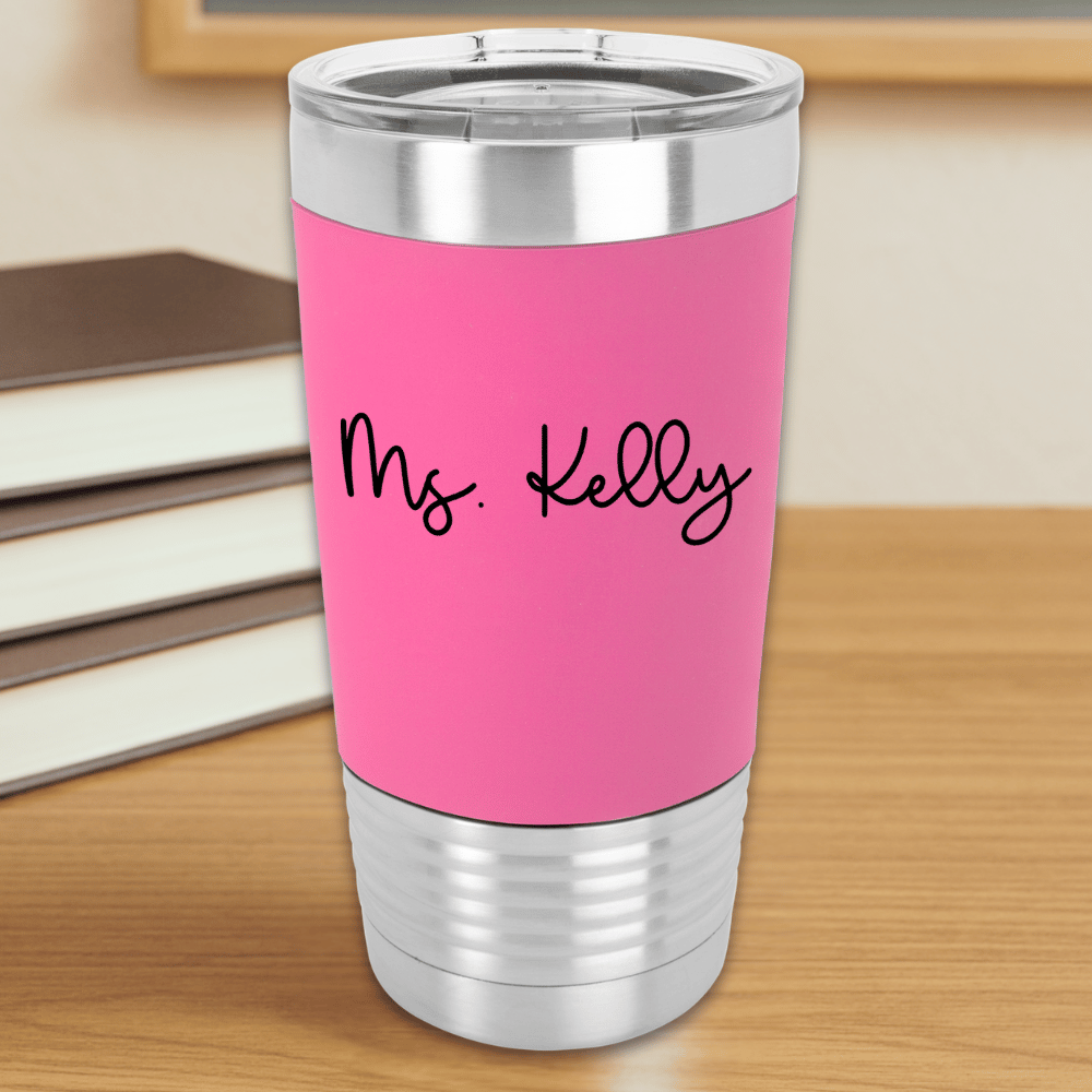 Pink insulated tumbler with 'Ms. Kelly' text engraved in black sitting on a wooden surface.