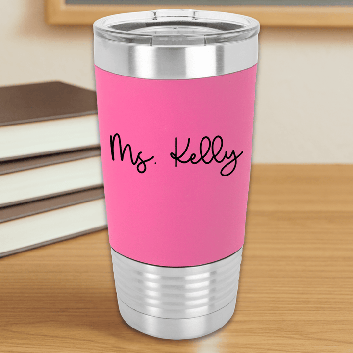 Pink insulated tumbler with 'Ms. Kelly' text engraved in black sitting on a wooden surface.