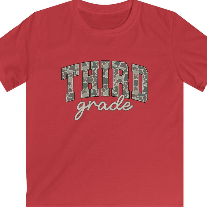 A red short-sleeve t-shirt with 'THIRD grade' printed on the chest. The word 'THIRD' is in a green and gray camouflage pattern, while 'grade' is written below in a tan cursive font.