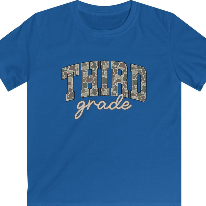 A royal blue short-sleeve t-shirt with a graphic on the chest reading 'THIRD grade' in camouflage block letters and beige script, shown on a plain tan background.