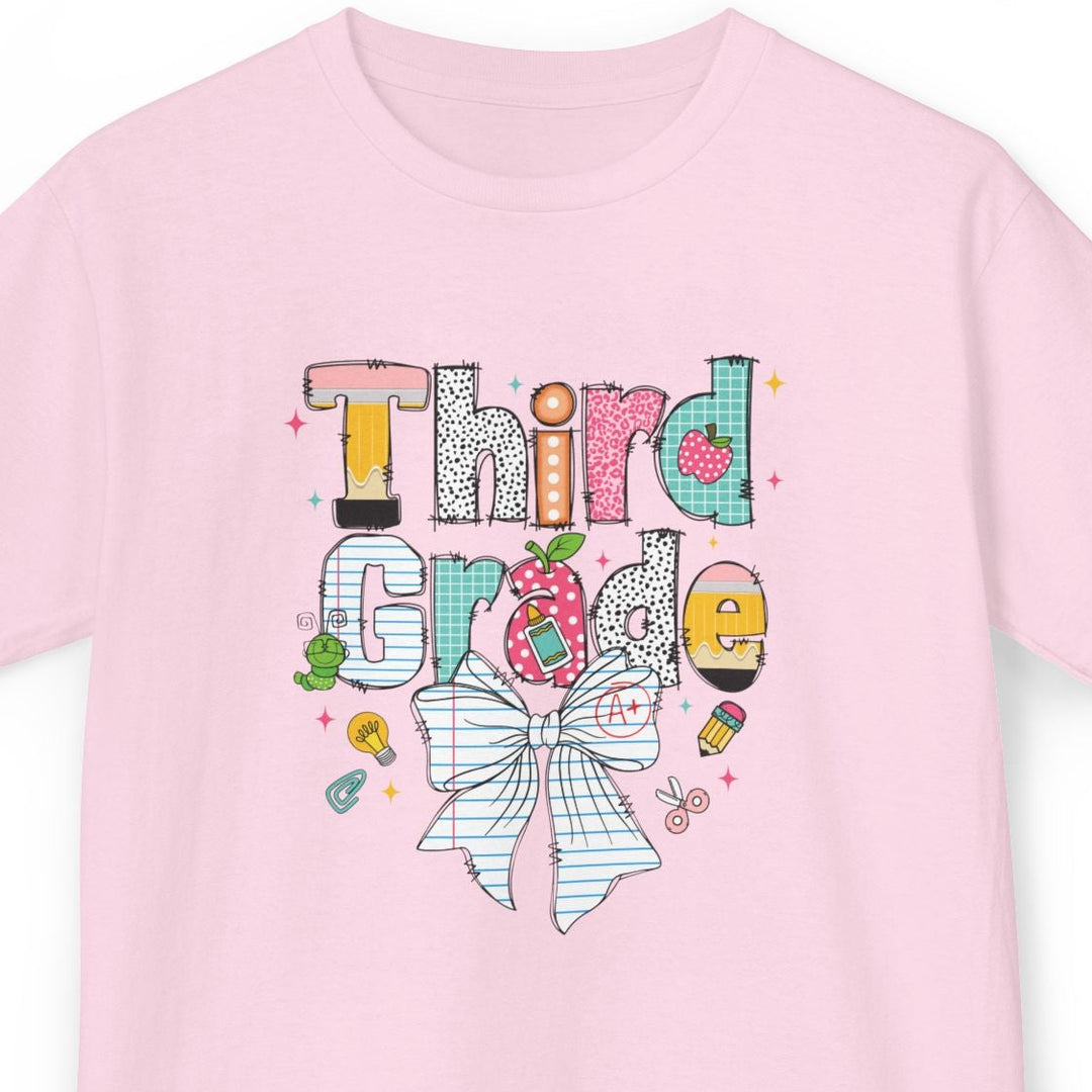 A light pink short-sleeve t-shirt with a colorful graphic on the front that reads 'Third Grade' in a playful, hand-drawn style with a striped bow illustration below, shown against a plain white background.
