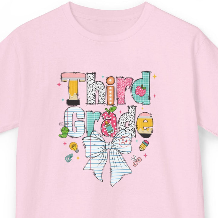 A light pink short-sleeve t-shirt with a colorful graphic on the front that reads 'Third Grade' in a playful, hand-drawn style with a striped bow illustration below, shown against a plain white background.