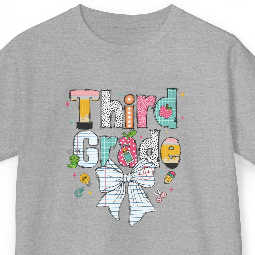 A heather gray short-sleeve t-shirt with a colorful graphic on the front that reads 'Third Grade' in stylized lettering, decorated with a large bow, pencil, and school-themed doodles, shown on a plain white background.