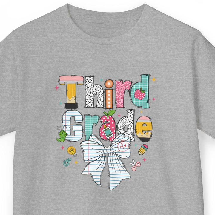 A heather gray short-sleeve t-shirt with a colorful graphic on the front that reads 'Third Grade' in stylized lettering, decorated with a large bow, pencil, and school-themed doodles, shown on a plain white background.