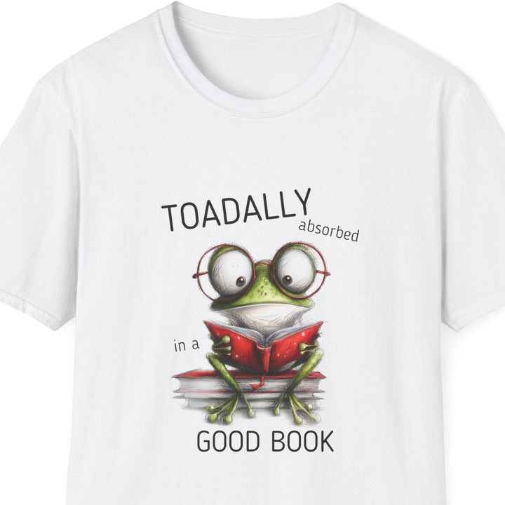 A white short-sleeve crewneck t-shirt featuring a cartoon graphic of a green frog wearing glasses and reading a red book, with the text 'TOADALLY absorbed in a' above and 'GOOD BOOK' below.