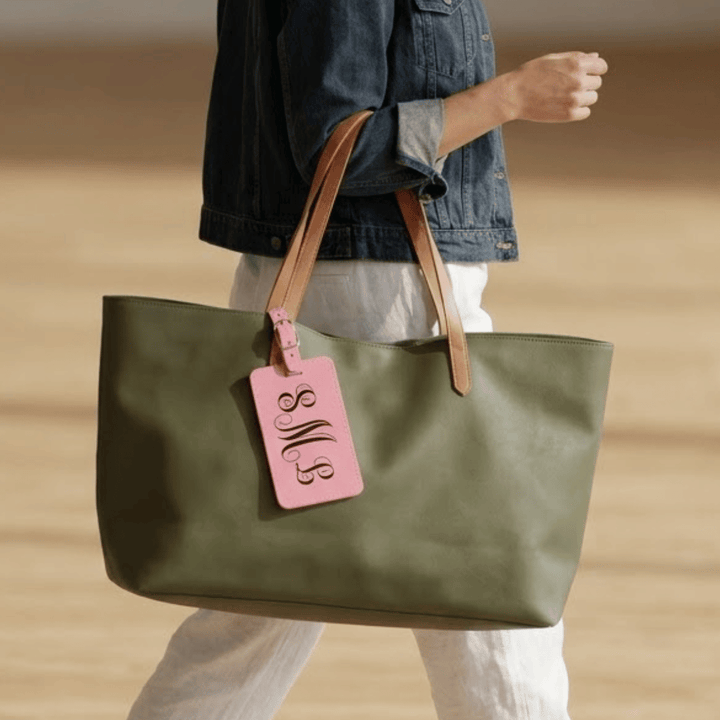 Person holding a green tote bag with a pink luggage tag against a beige background