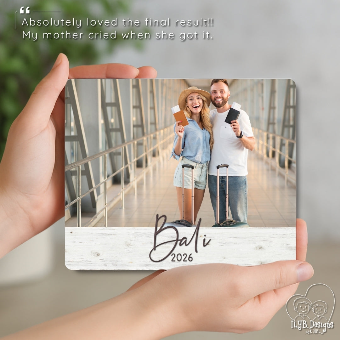 Hand holding a photo board with a couple in Bali 2026 on a wooden surface.