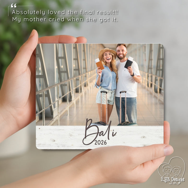 Hand holding a photo board with a couple in Bali 2026 on a wooden surface.