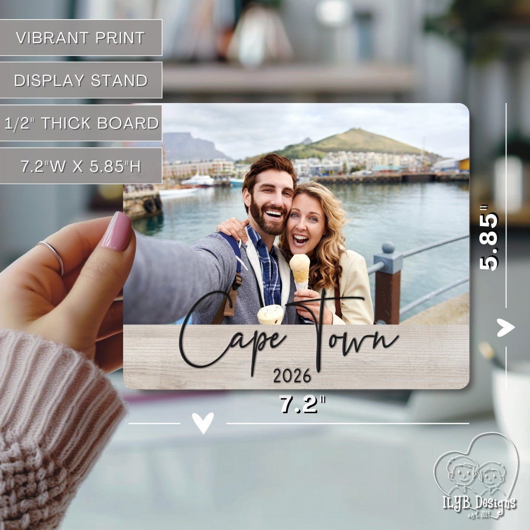 Hand holding a wooden board with a printed photo of a couple in Cape Town, 2026, with product details overlayed.