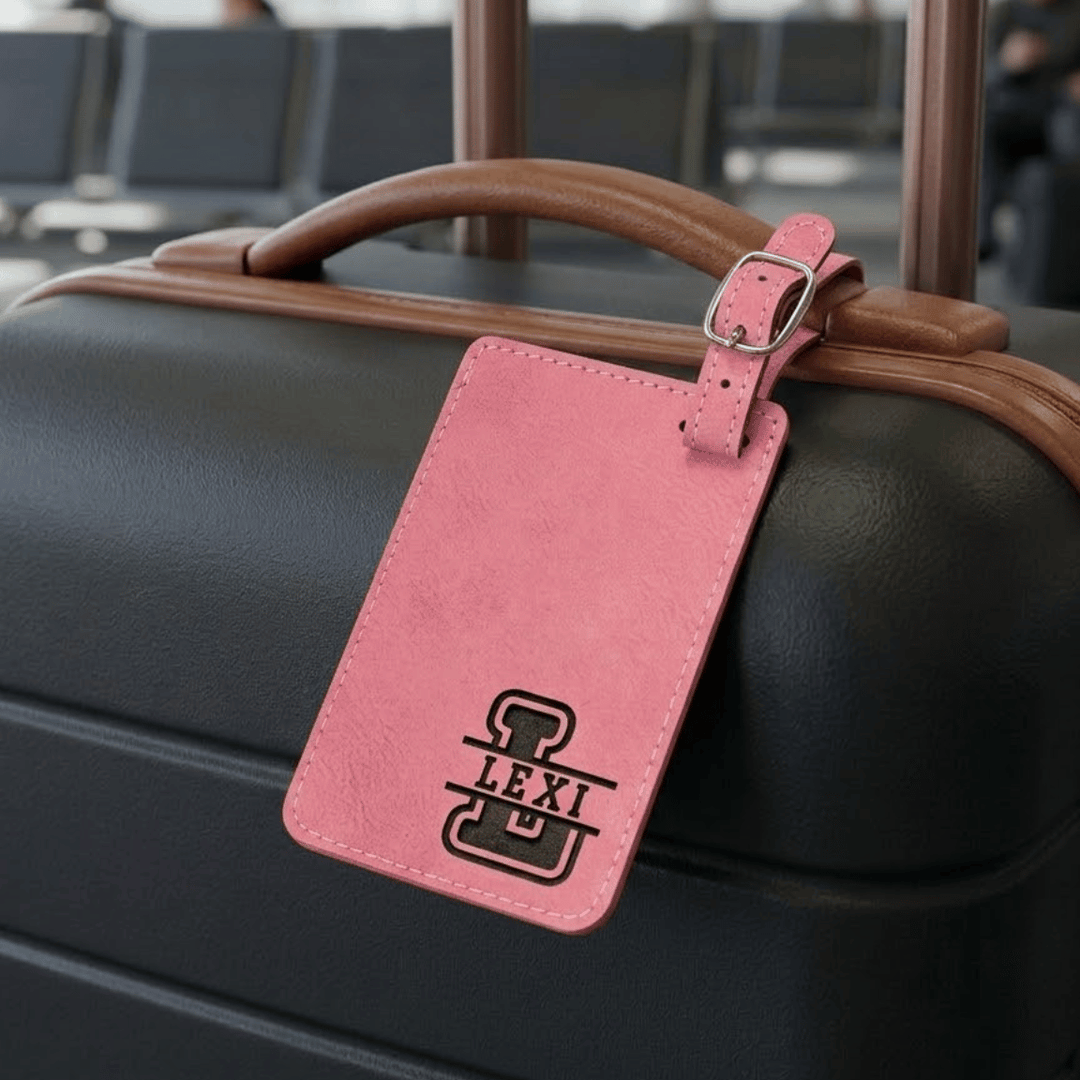 Black suitcase with a pink luggage tag monogrammed with 'LEXI' in an airport setting.