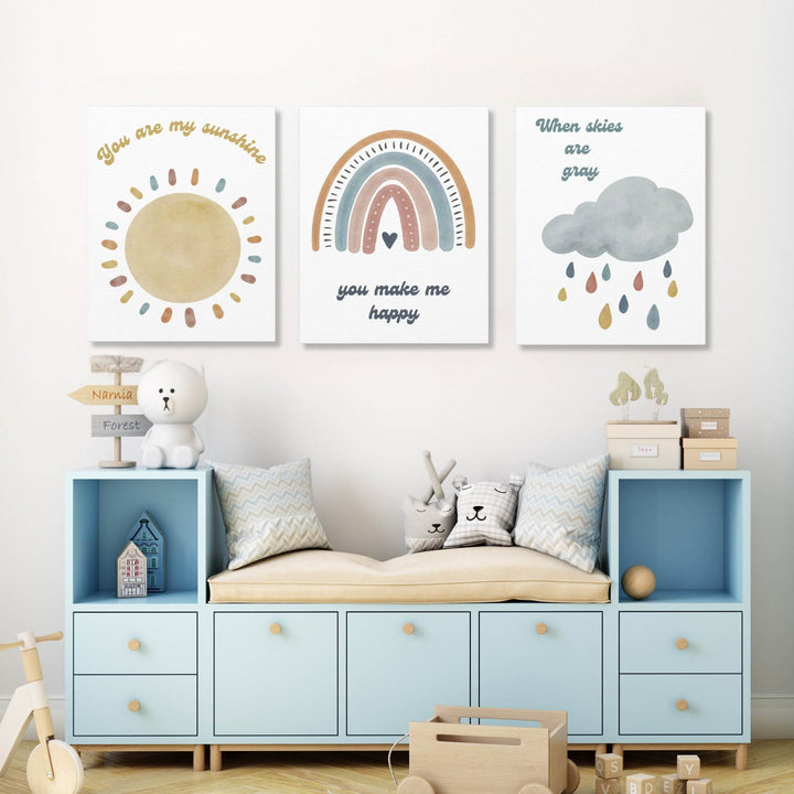 Children's room with set of 3 colorful wall art canvases each with separate text, 'your are my sunshine', 'you make me happy', and 'when skies are gray' above a blue storage unit.