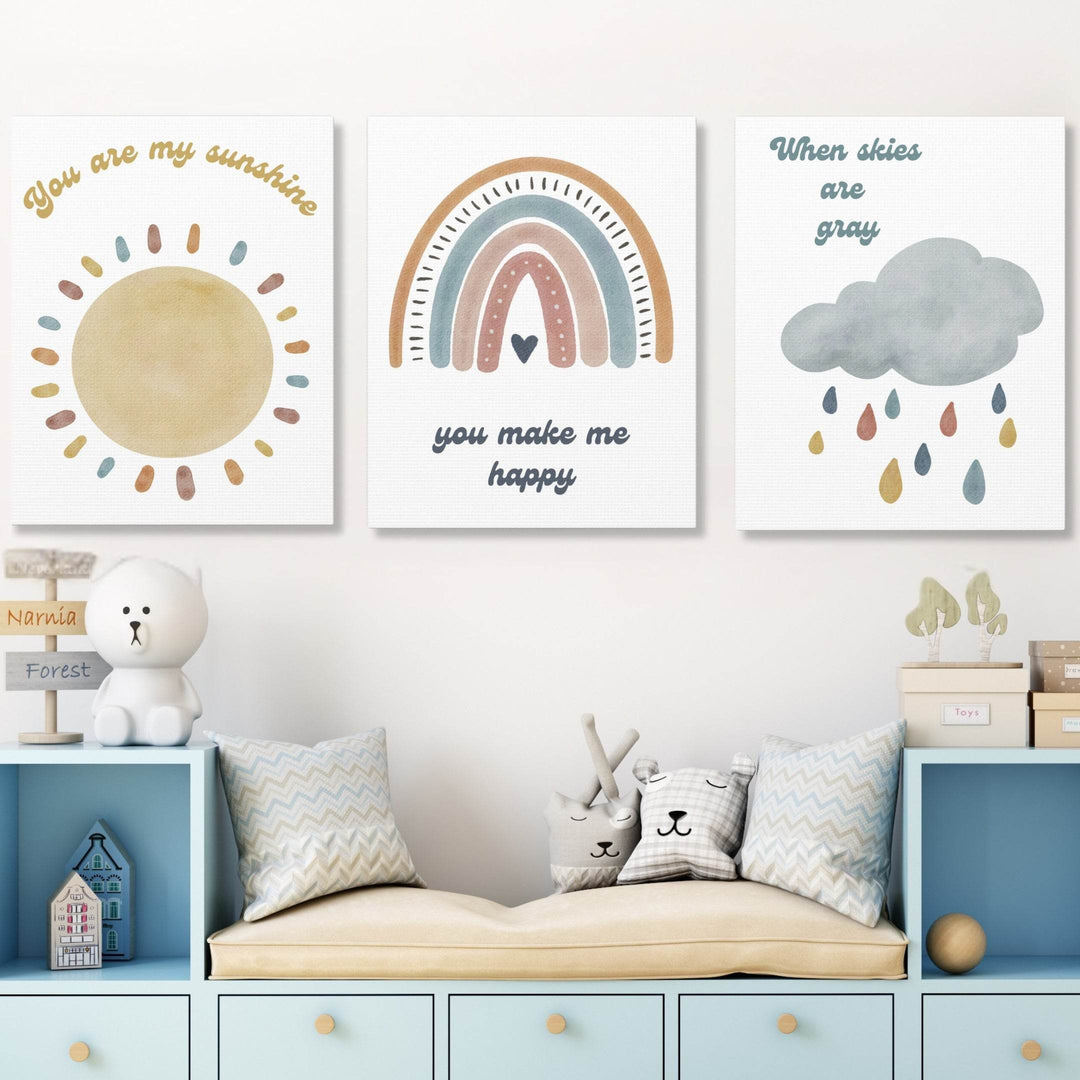 Three wall canvases with a watercolor sun, rainbow, and cloud boho design in a child's room.