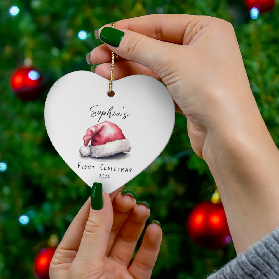 Heart-shaped ornament with baby in Santa hat design held by hands against a Christmas tree background