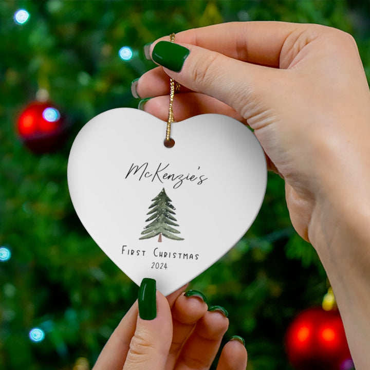 Heart-shaped ornament with 'McKenzie's First Christmas 2024' text against a Christmas tree background.