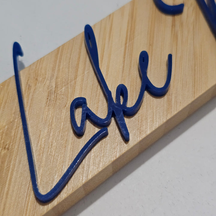 A close-up of a bamboo picture frame featuring the word "Lake" in raised blue cursive acrylic lettering on a light natural wood background.